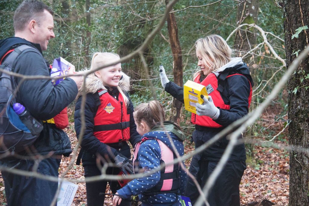 Two adults and two kids in the woods with lifejackets over their coats.