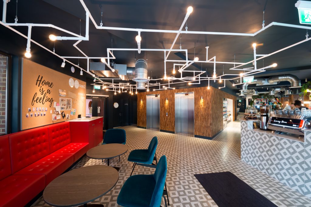 Large hotel lobby with a seating area to the left, elevators, and a bar to the right.
