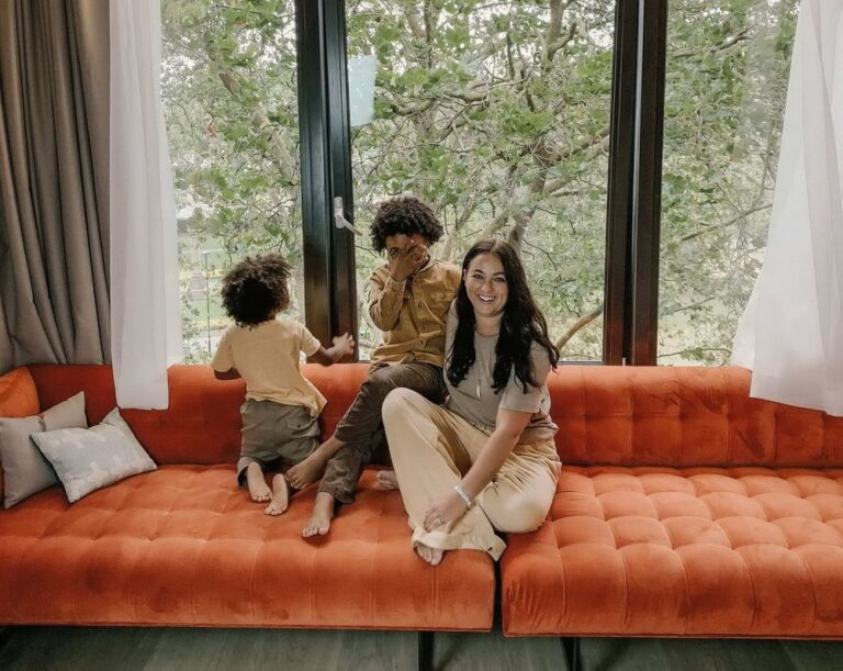 A woman and two kids sit on a large couch in front of a wall of windows in room2 Southampton.